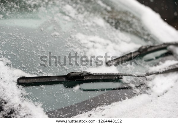 Car wiper blades clean snow from car\
windows. Flakes of snow covered the car with a thick layer. Safe\
driving with working wipers and clean\
windshield.