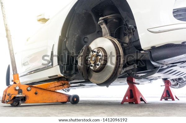 Car without wheel on car jack with car stands\
for safety in repair shop\
background.