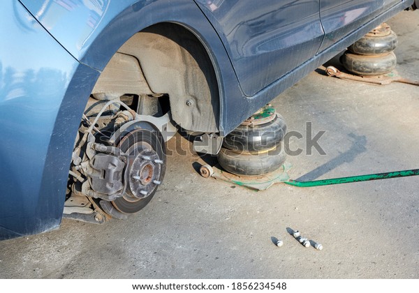 Car without wheels lifted\
up with jacks during wheel replacement. Seasonal change of car\
tires.