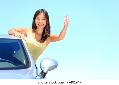 Car. Woman Driver Happy Smiling Showing Thumbs Up Coming Out Of Car Window On Blue Summer Sky Above The Clouds. Beautiful Young Mixed Race Caucasian / Chinese Asian Woman.