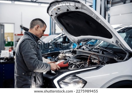 A car workshop worker is doing car battery diagnostics with special device.