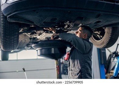 A car workshop worker is draining oil from engine while standing under the car. - Powered by Shutterstock