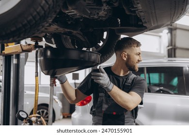 A car workshop worker is draining oil from engine while standing under the car - Powered by Shutterstock