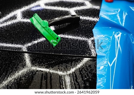 Car wrap tools, including squeegees and magnets on wet car hood. Car detailing tools to shape PPF wrap during installation for smooth coverage. PPF Paint Protection Film Tools on Car Hood