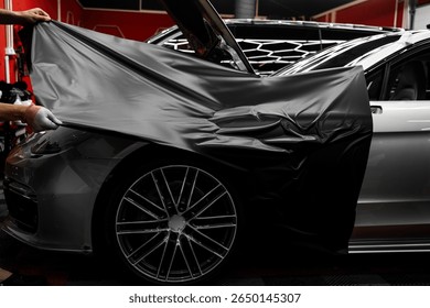 Car wrapping process using black matte vinyl stretched into place. Careful application and tensioning of black vinyl avoids surface damage or bubbling. Matte black vinyl is applied across car hood