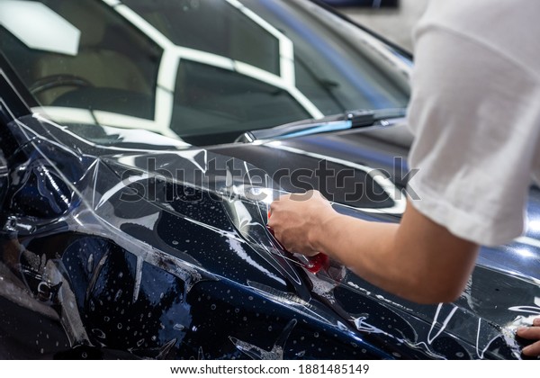 Car wrapping specialist cutting vinyl\
transparent film for protection car paint focus on hand holding\
cutting tools. Protective film. Car paint\
protection