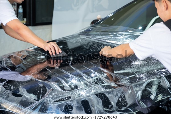 Car wrapping specialist putting a transparent\
vinyl film on car hood. Applying a protective film to the car to\
protect car paint.
