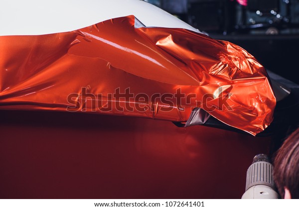 Car wrapping specialist putting vinyl\
foil or film on car. cutting protective film with torch. wrapping\
yacht, boat, ship, car, mobile home. orange\
film