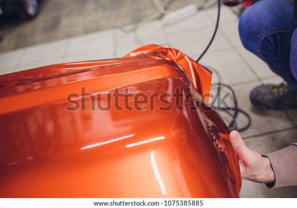 Car wrapping specialist putting vinyl foil or\
film car wrapping protective film yacht, boat, ship, car, mobile\
home. orange film heating with hair dryer and trimming plastic soft\
hard squeegee