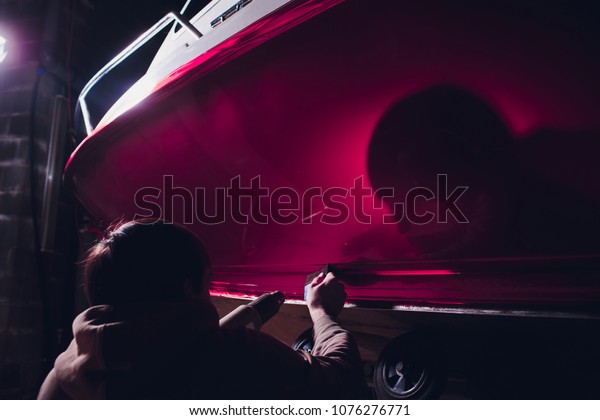 Car wrapping specialist putting vinyl foil or\
film car wrapping protective film yacht, boat, ship, car, mobile\
home. pink red film heating with hair dryer and trimming plastic\
soft hard squeegee