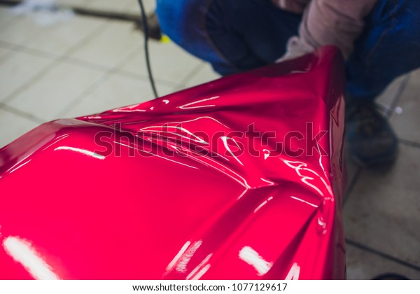 Car wrapping specialist putting vinyl foil or\
film on car wrapping protective film yacht, boat, ship, car, mobile\
home. pink red film hand\
pulls