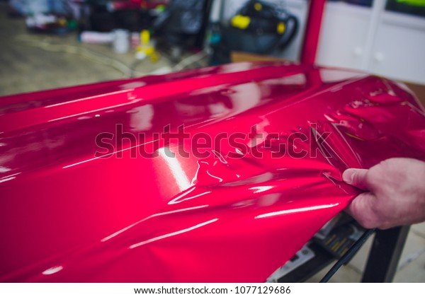 Car wrapping specialist putting vinyl foil or\
film on car wrapping protective film yacht, boat, ship, car, mobile\
home. pink red film hand\
pulls