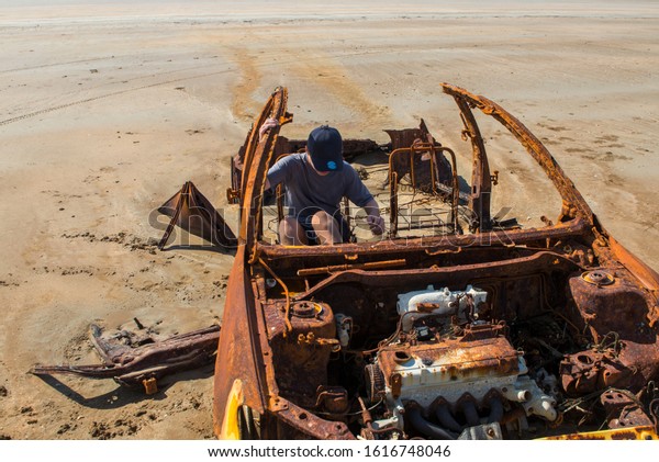 A car wreck that has been abandoned on the beach\
after being caught in a rising tide. The photo is landscape and\
shows the vehicle partially buried in the sand on a beach with a\
low tide.