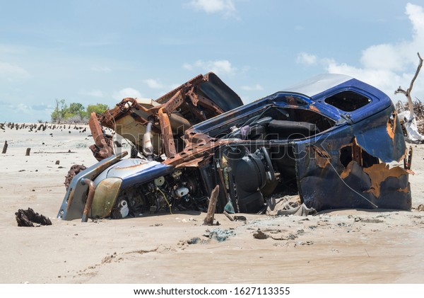 A car\
wreck that has been abandoned on the beach after being caught in a\
rising tide. Shows the vehicle partially buried in the sand on a\
beach with a low tide and partly cloudy day.\
