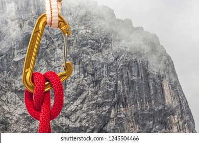 A carabiner with a climbing rope and sling on rock wall background. Mountaineering and climber safety equipment detail close up shot.