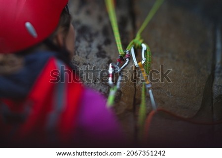 Carabiners and safety ropes against the background of a rock and a climber standing at the station, blurred image with an emphasis on the climbing equipment, close-up, no face visible. Selected focus.