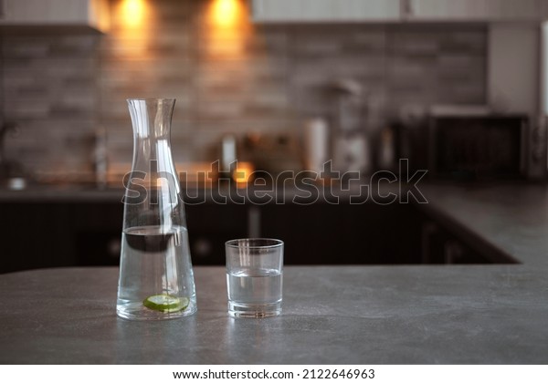 carafe with detox water and a glass on the table\
in the kitchen