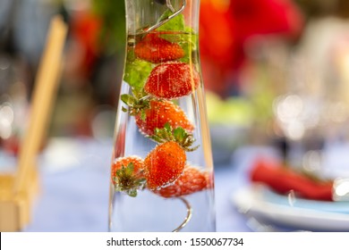 a carafe filled with water and strawberries stands on a served blue table.  close up, soft focus. served table is on background in blur 