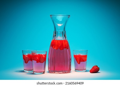 Carafe and glasses with strawberry lemonade on a turquoise background