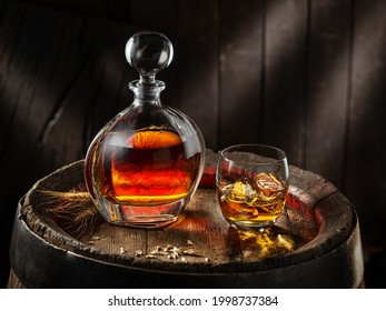 Carafe of whisky and glass of whisky on old wooden cask at the dark background.