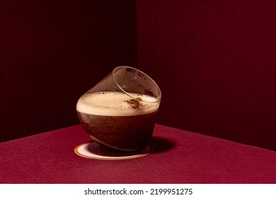 Carajillo Cocktail, Cold Coffee Drink On A Red Background Served In An Old Fashioned Glass With Cinnamon Stick Decoration