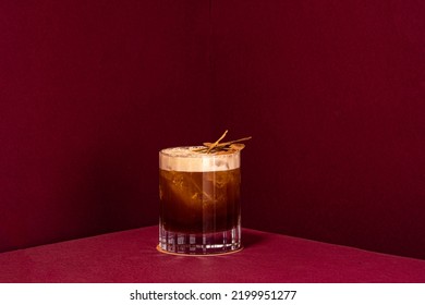 Carajillo Cocktail, Cold Coffee Drink On A Red Background Served In An Old Fashioned Glass With Cinnamon Stick Decoration