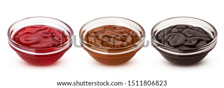 Caramel, chocolate sauces and red berry jam in glass bowls isolated on white background with clipping path, collection of sweet toppings for baking and ice cream