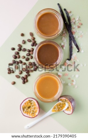Caramel sauce in glass jars. Passion fruit, vanilla sticks, coffee beans and jars with caramel on a light green background with copy space