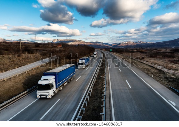 Caravan or convoy of lorry trucks on country highway\
under a dramatic sky