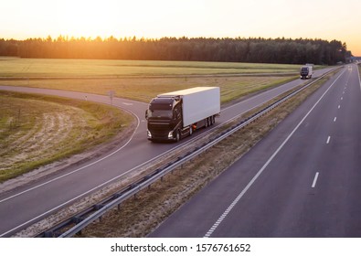A caravan of modern freight trucks transports cargo in the evening against the sunset. Trucks drive on the motorway in the evening