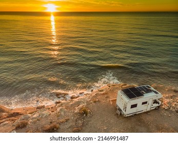 Caravan with solar panels on roof camping on coastal cliff at sunrise. Mediterranean sea in Spain.