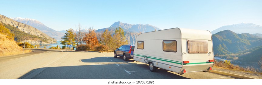 Caravan trailer, bicycle and car parked on a mountaintop with a view on French Alps near lake Lac de Serre-Poncon. Transportation, RV, motorhome, road trip, camping, tourism, recreation, lifestyle