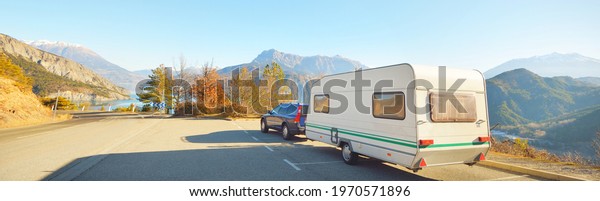 Caravan trailer, bicycle and car parked on a\
mountaintop with a view on French Alps near lake Lac de\
Serre-Poncon. Transportation, RV, motorhome, road trip, camping,\
tourism, recreation,\
lifestyle