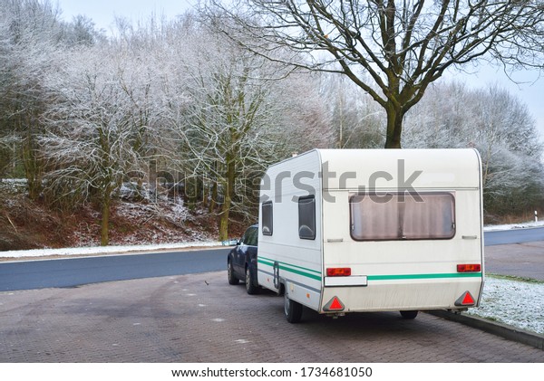 Caravan trailer and a car parked under\
the frosty tree. Bicycle road and city park in the background.\
Germany. Christmas vacations, recreation\
theme