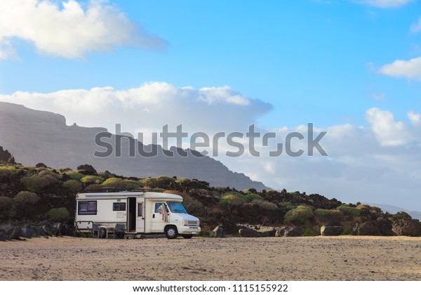 Caravan trailer parked\
on a beach with mountains view on Canary island. Summer vacation.\
Travel concept.