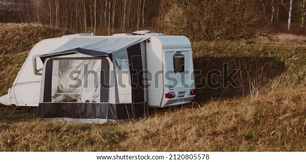 Caravan trailer parked on a green lawn in a\
small village on a clear spring day. Normandy, France.\
Transportation, RV, motorhome, road trip, local travel, ecotourism,\
recreation, leisure\
activity