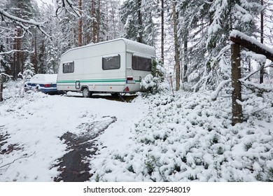 Caravan trailer parked in a snow-covered evergreen pine forest. First snow in autumn, early winter. Finland. Camping, ecotourism, vacations, weekend getaway, road trip themes
