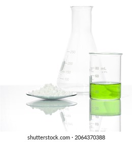 Carbamide In Chemical Watch Glass And Iron (II) Sulfate Liquid In Beaker Place Next To Erlenmeyer Flask On White Laboratory Table. Side View