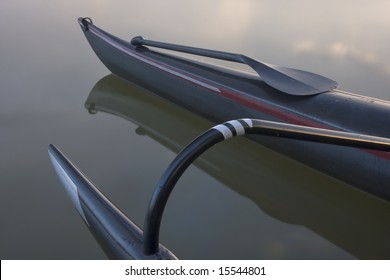Carbon fiber bent shaft paddle on a slim bow of racing outrigger canoe, calm lake.