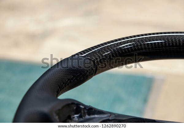 \
\
Carbon steering wheel of a black car in the\
workshop tightened and stitched perforated with natural leather\
close up.\
