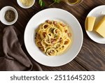 Carbonara pasta, spaghetti with crisp pancetta and black pepper on white plate over rustic wooden background. Traditional italian cuisine. Top view, flat lay