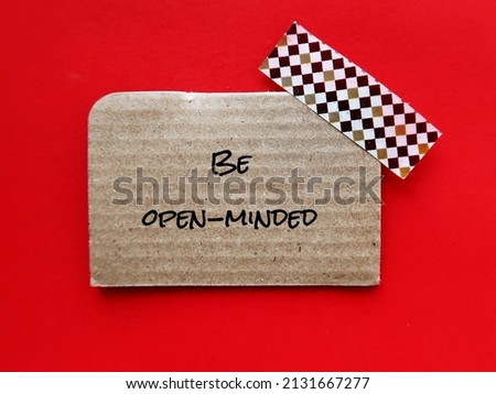 Card board on red background with text BE OPEN-MINDED, means being receptive to a wide variety of ideas, arguments, and information, change incorrect beliefs, learning and personal growth
