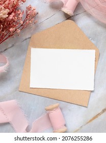 A card and envelope on marble with dried pink flowers and silk ribbons top view. Flat lay with horizontal blank card. Romantic Thank you or rsvp card mockup, copy space
