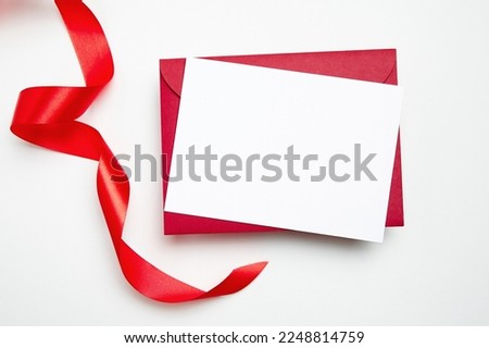 Card mockup, blank flyer with red ribbon on white background, top view, flat lay. Blank invitation, holiday greeting card mockup with copy space