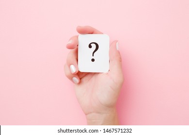 Card of question mark in young woman hand on pastel pink background. Concept of plans, thoughts or other good ideas for making decision. Closeup.