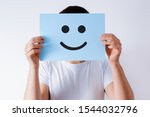 Card with a smiley face on the background of a man. The concept of satisfaction, covering real emotions with artificial ones. Blue card with a smiley face.