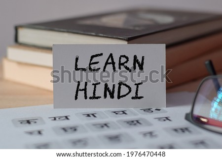A card with the text LEARN HINDI on wooden desk with hindi alphabet letters. New language learning concept, selective focus on the card. 