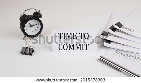 Card with text TIME TO COMMIT on a white background, near office supplies and alarm clock. Business