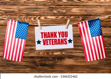 card with thank you veterans lettering hanging on string with pins and american flags on wooden background - Shutterstock ID 1346321462