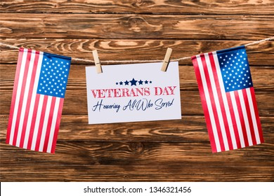 card with veterans day lettering hanging on string with pins and american flags on wooden background - Shutterstock ID 1346321456
